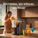 Mujer sirviendo jugo en máquina de granizados Avera de 1.6L con control táctil y vasos de frappés en barra.