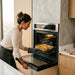Mujer usando el horno empotrable Avera a gas con control táctil para cocinar verduras con la función de convección.