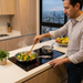 Una persona cocina en una Parrilla Inducción Avera de 2 quemadores empotrada en una cocina moderna, con sartenes y pantalla LED encendida.