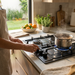 Persona cocinando en la Parrilla de Gas Avera de 3 Quemadores en acero negro, en una cocina moderna y luminosa.